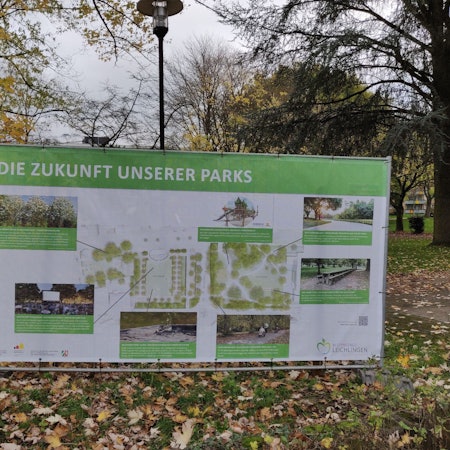Ein großes Transparent mit Fotos, Planskizzen und Erläuterungen zur Umgestaltung steht an der Baustelle im Leichlinger Stadtpark.