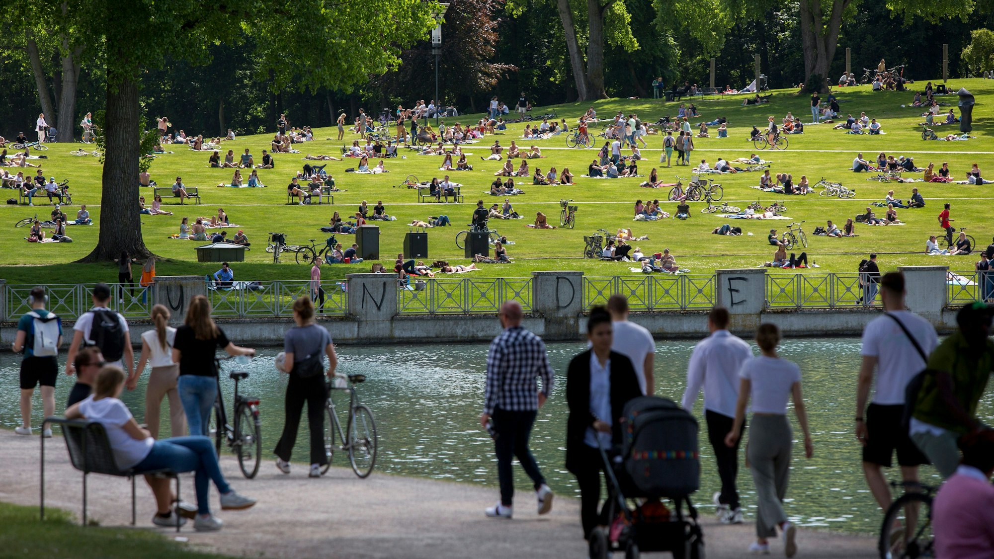 Menschen spazieren und sonnen sich am Aachener Weiher in Köln.