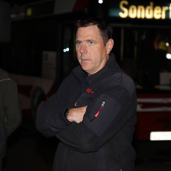 Feuerwehrchef Jörg Köhler steht im Dunkeln mit verschränkten Armen vor einem Bus, dessen Anzeige „Sonderfahrt“ anzeigt. Im Hintergrund steht Bürgermeister Frank Stein.