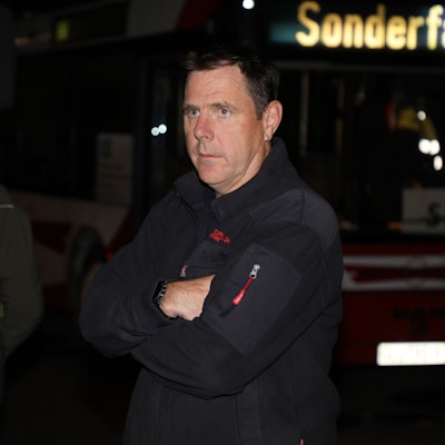 Feuerwehrchef Jörg Köhler steht im Dunkeln mit verschränkten Armen vor einem Bus, dessen Anzeige „Sonderfahrt“ anzeigt. Im Hintergrund steht Bürgermeister Frank Stein.