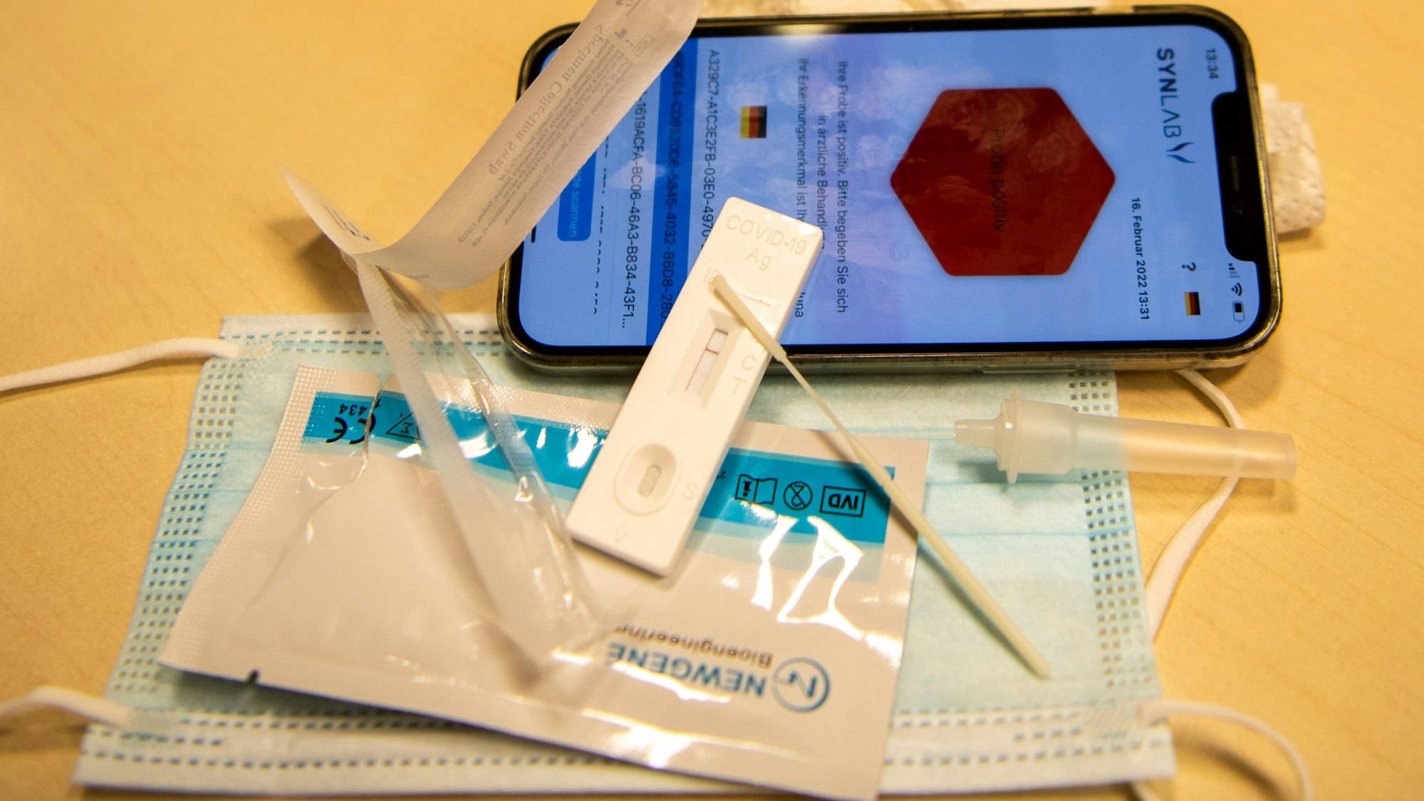 Corona-Tests und Masken und ein Handy liegen auf einem Tisch.