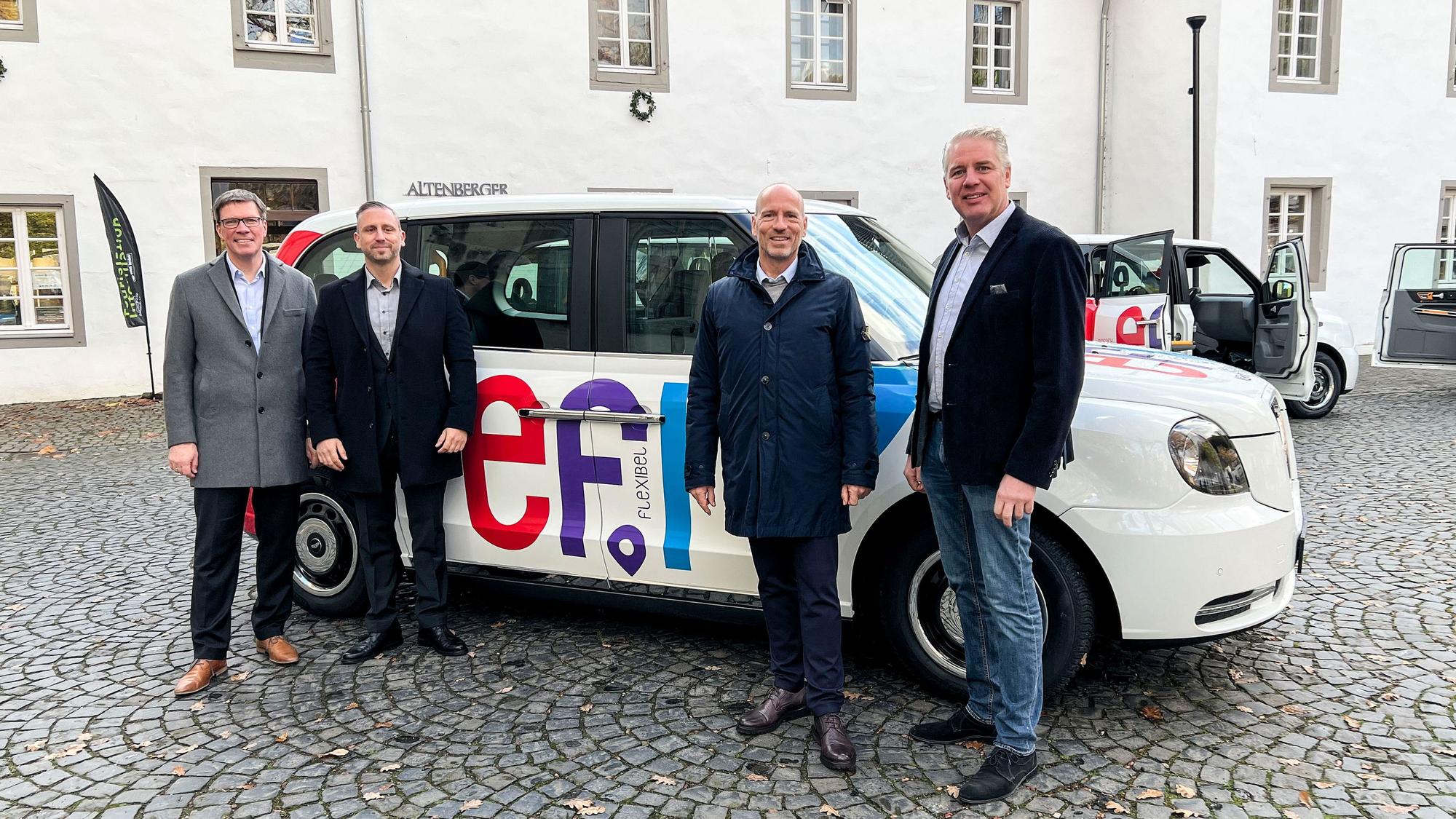 Landrat Stephan Santelmann, Georg Königsmann vom Unternehmen Clevershuttle, Wupsi-Chef Marc Kretkowski und Bürgermeister Robert Lennerts stehen an einem der neuen Efi-Großraumtaxis.