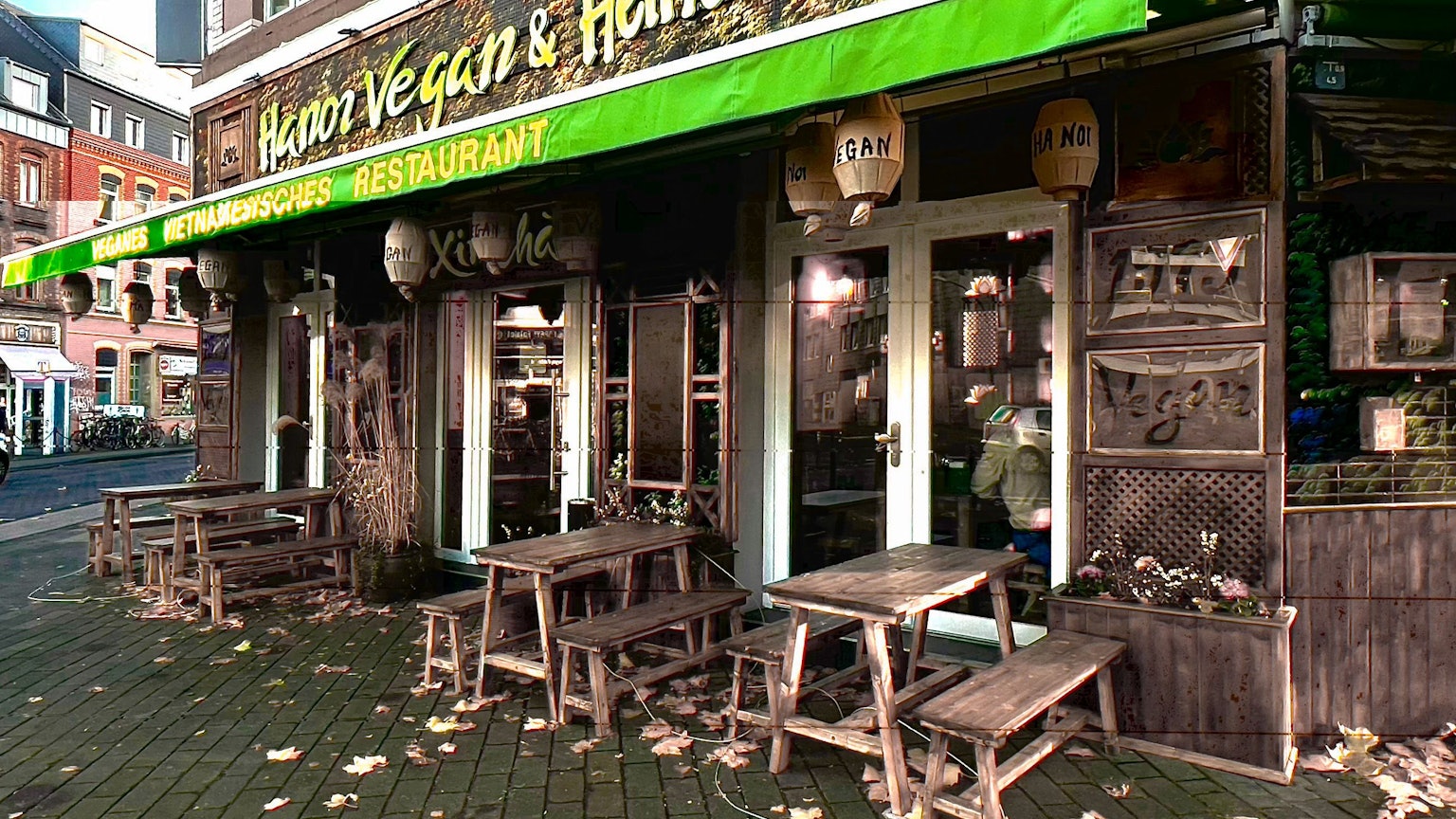 Eine grüne Markise hängt an einem Eckhaus, das eine asiatisch anmutende Fassade mit Holzornamenten hat.