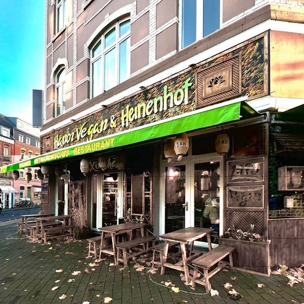 Eine grüne Markise hängt an einem Eckhaus, das eine asiatisch anmutende Fassade mit Holzornamenten hat.