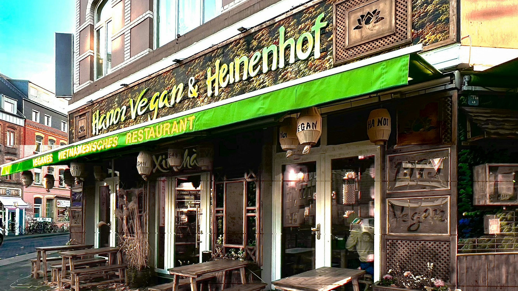 Eine grüne Markise hängt an einem Eckhaus, das eine asiatisch anmutende Fassade mit Holzornamenten hat.