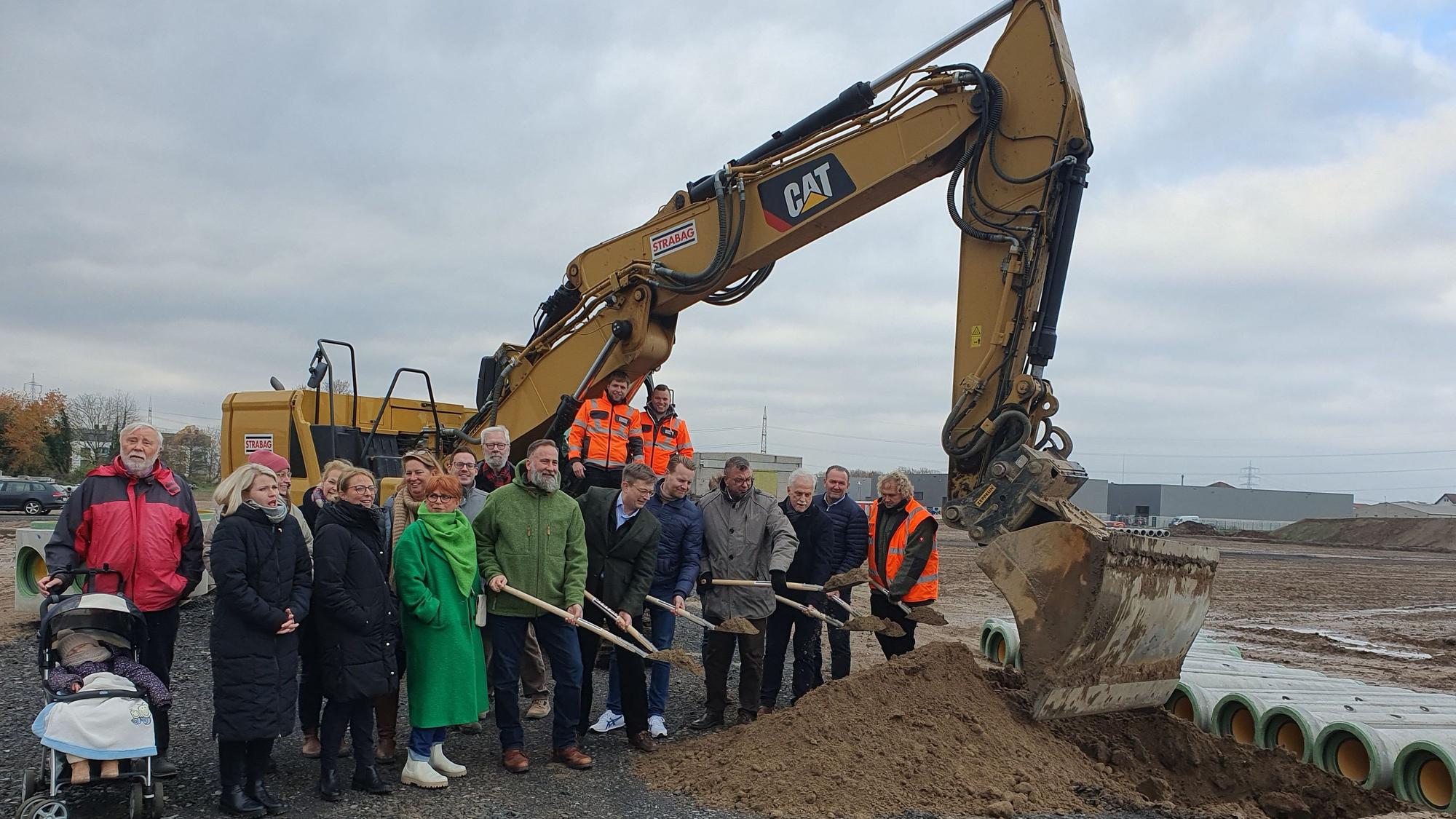 Vertreter von Politik, Stadtverwaltung und Niederkasseler Stadtentwicklunsgesellschaft stehen an der Baustelle für ein neues Wohnviertel.