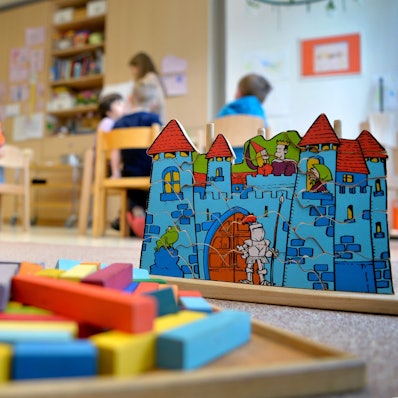 Spielzeug liegt in einer Kindertagesstätte auf dem Boden. Im Hintergrund sind Kinder zu erkennen.