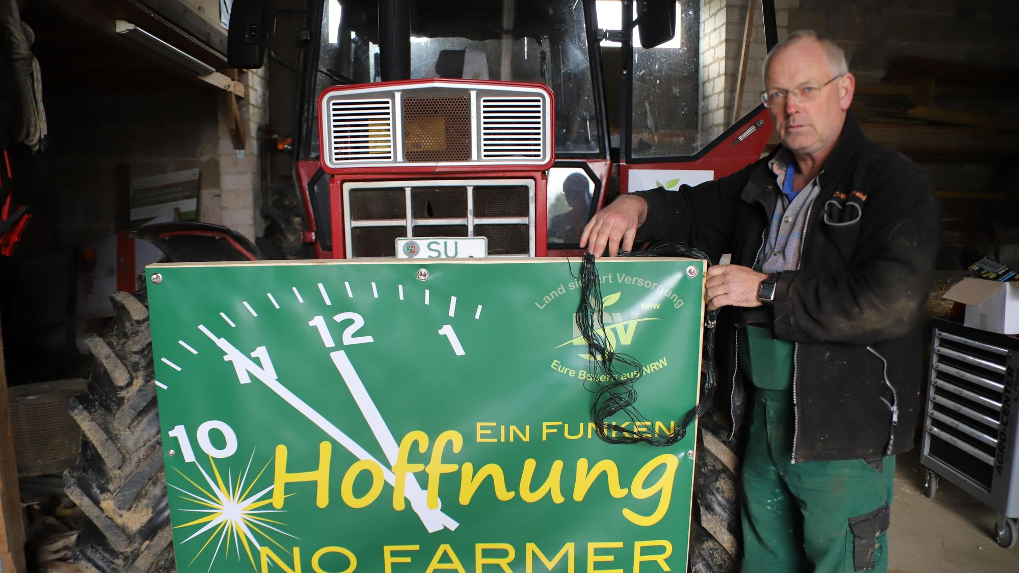 Ein Landwirt steht mit einem Protestschild vor einem Traktor.