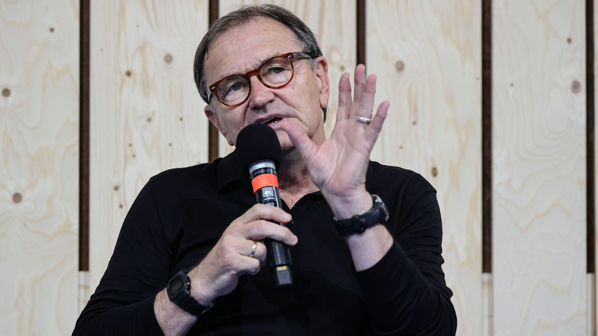 Ewald Lienen, ehemaliger Fußballprofi und Trainer, äußert sich gestikulierend mit einem Mikrofon in der Hand.