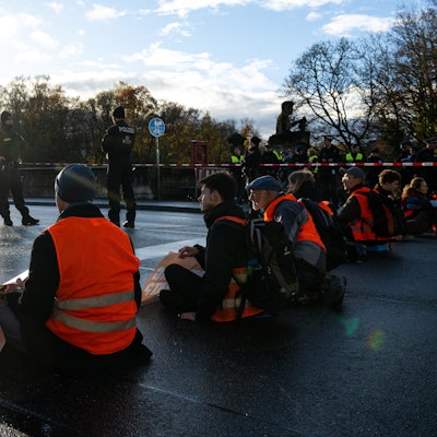 In einer Reihe sitzen Klimaaktivisten der Umweltschutzbewegung „Letzte Generation“ sitzen auf der Münchner Prinzregentenstraße und blockieren den Verkehr.