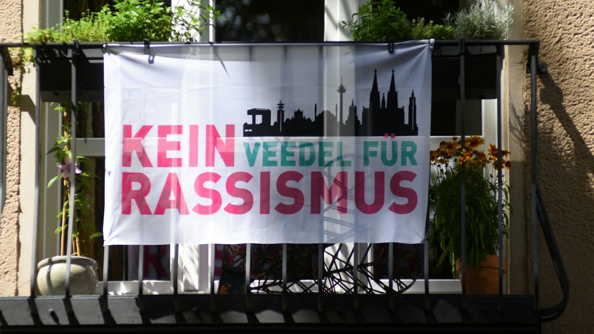 Eine Fahne mit der Aufschrift "Kein Veedel für Rassismus" hängt an einem Balkon am Rathenauplatz.