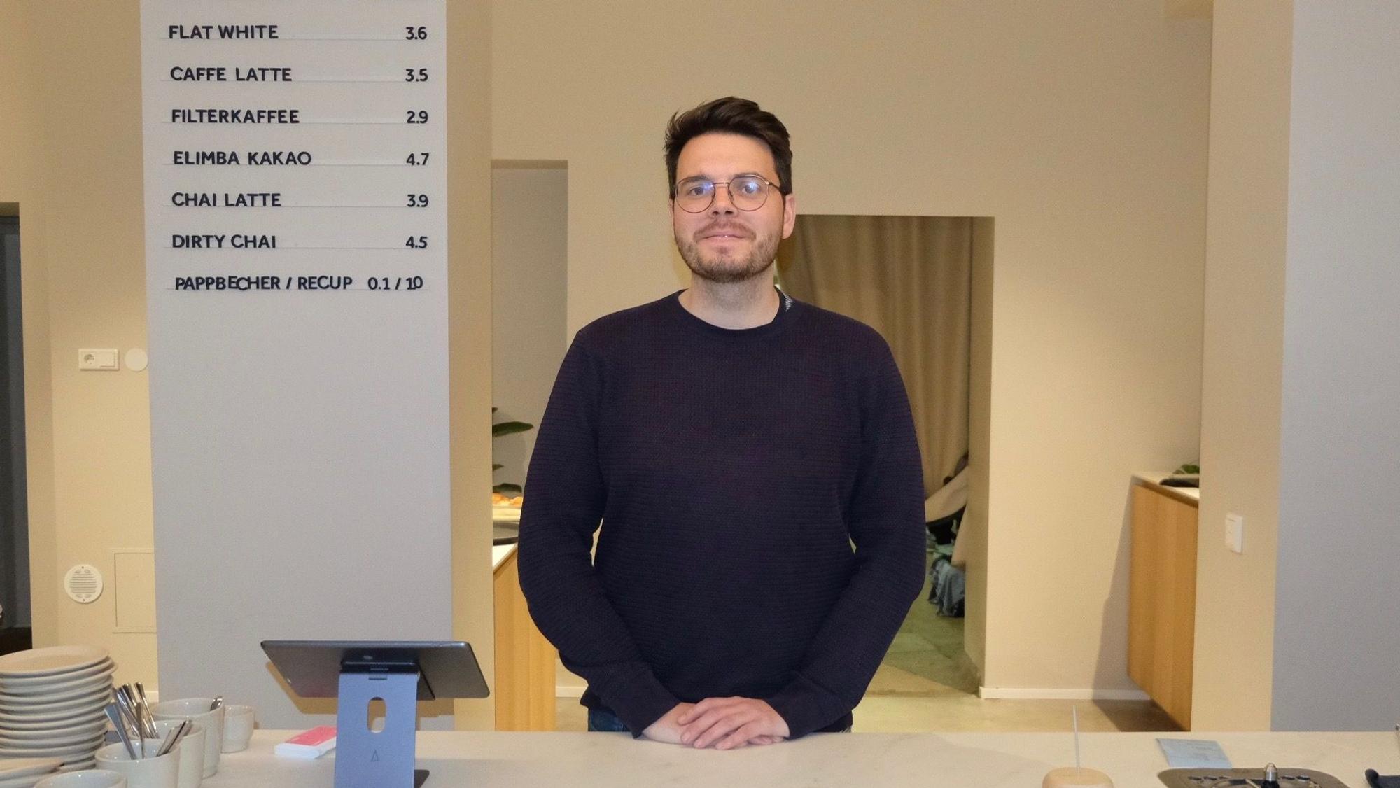Ein dunkelhaariger Mann mit Brille steht hinter einem weißen Verkaufstresen.