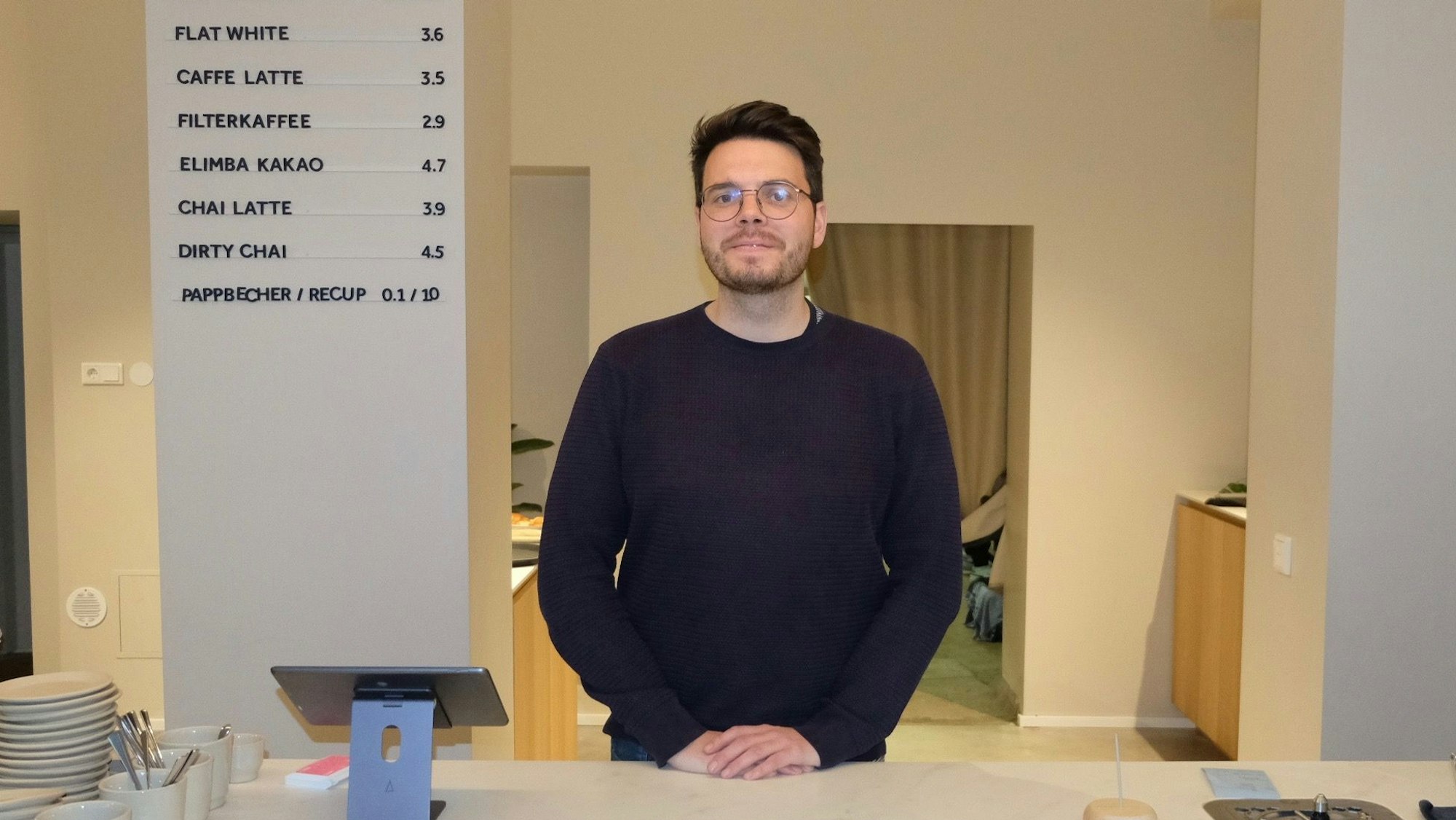 Ein dunkelhaariger Mann mit Brille steht hinter einem weißen Verkaufstresen.