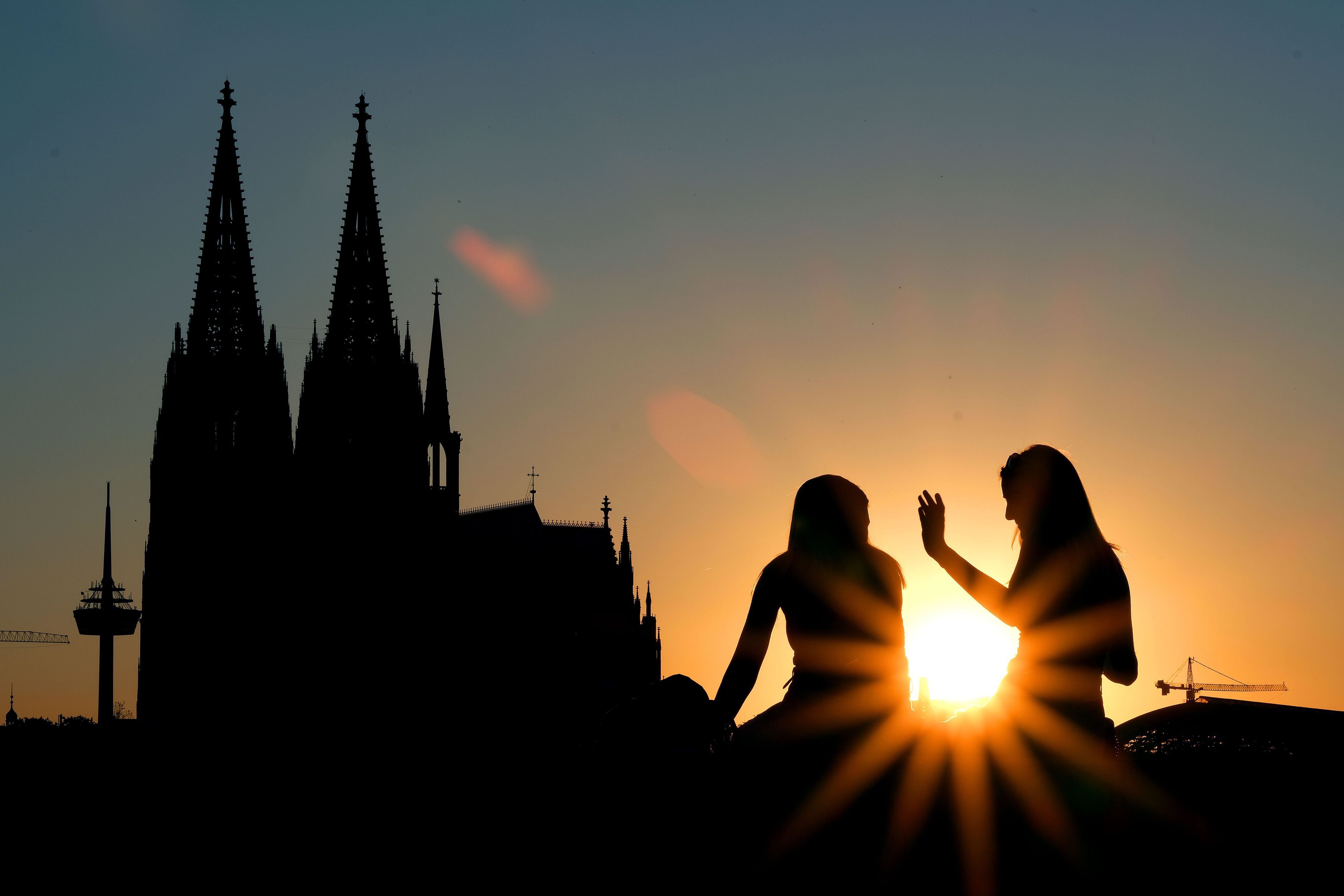 Zwei Frauen sitzen im Sonnenuntergang am Rheinboulevard vor dem Dom.