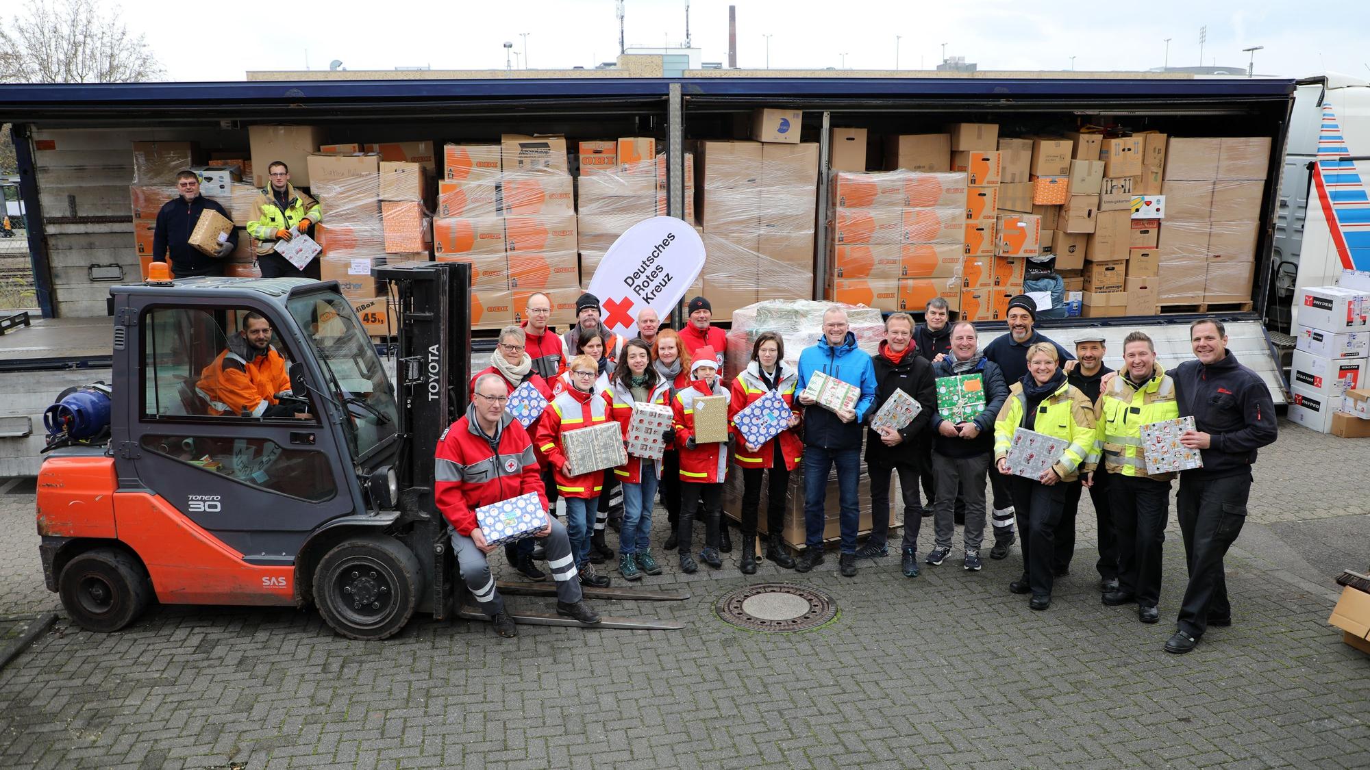 Menschen mit Geschenken und Kartons stehen vor einem beladenen, fast vollen Lastzug.