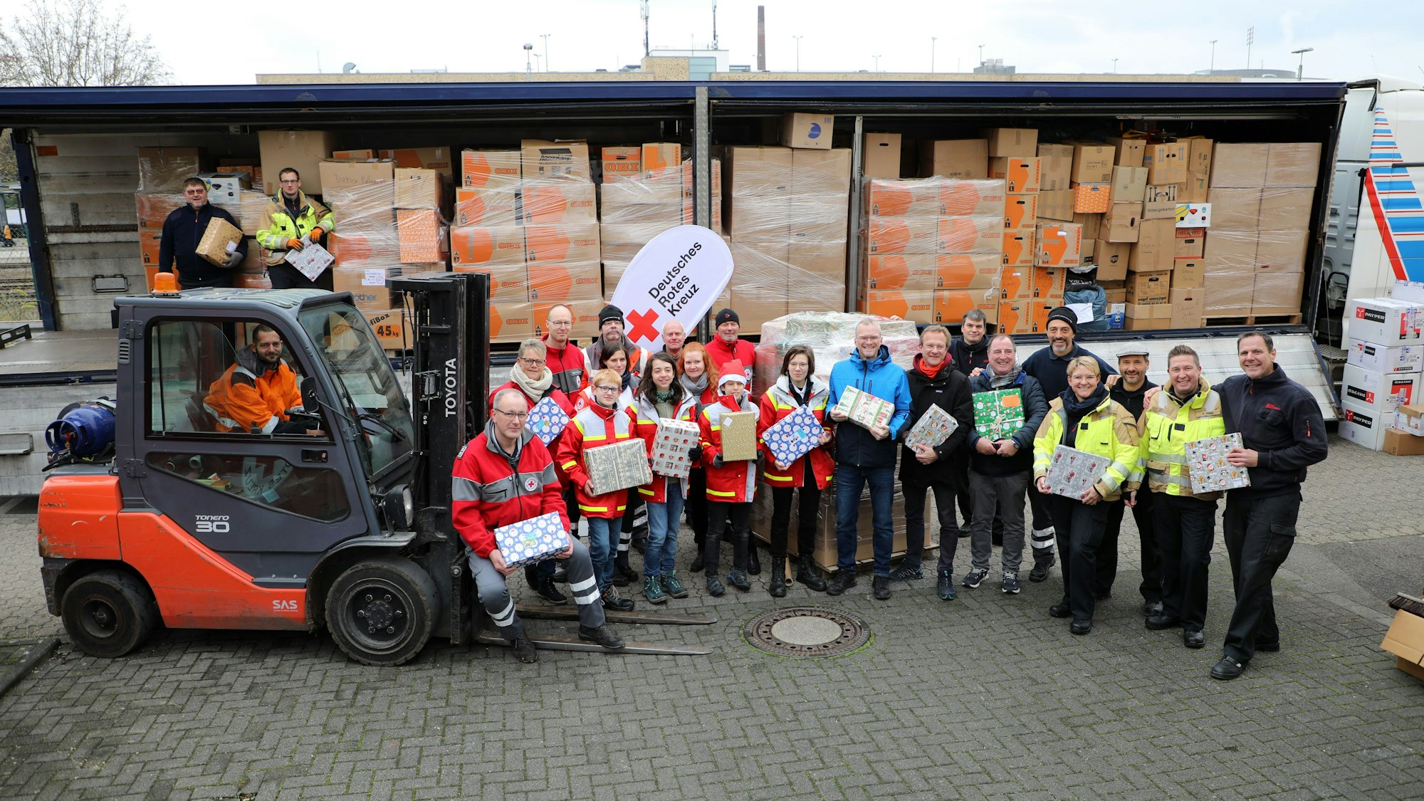 Menschen mit Geschenken und Kartons stehen vor einem beladenen, fast vollen Lastzug.