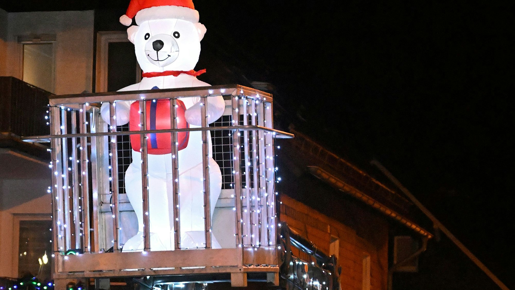 Ein leuchtender Schneebär mit Zipfelmütze steht im Korb auf eine Auslieger eines Traktors.