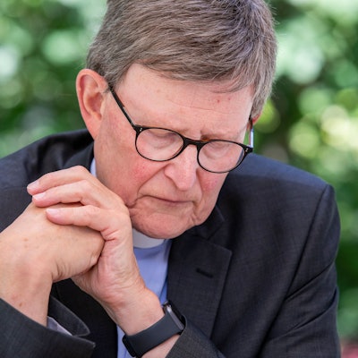 Der Kölner Erzbischof, Kardinal Rainer Woelki, sitzt mit gesenktem Blick und ineinander geschlagenen Händen im Garten des erzbischöflichen Hauses.