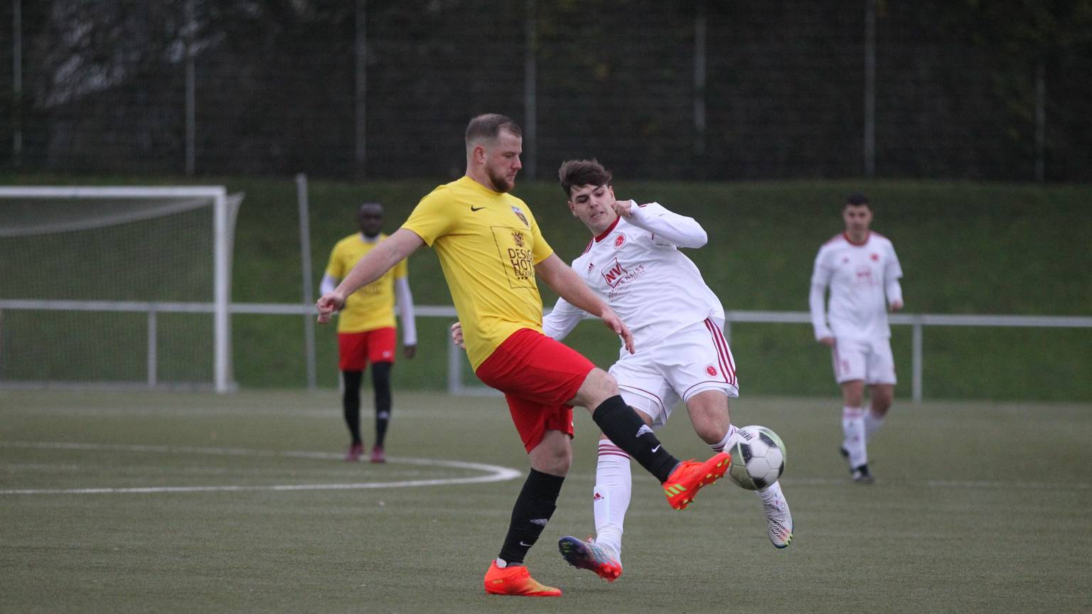Ein Euskirchener Spieler in einem gelb-roten Trikot schießt den Ball aus der Gefahrenzone.