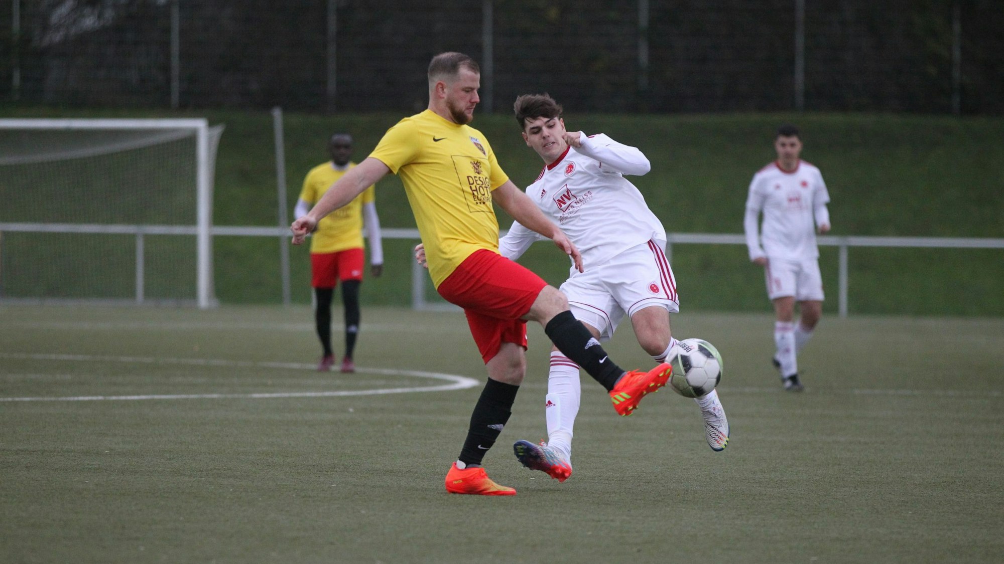 Ein Euskirchener Spieler in einem gelb-roten Trikot schießt den Ball aus der Gefahrenzone.