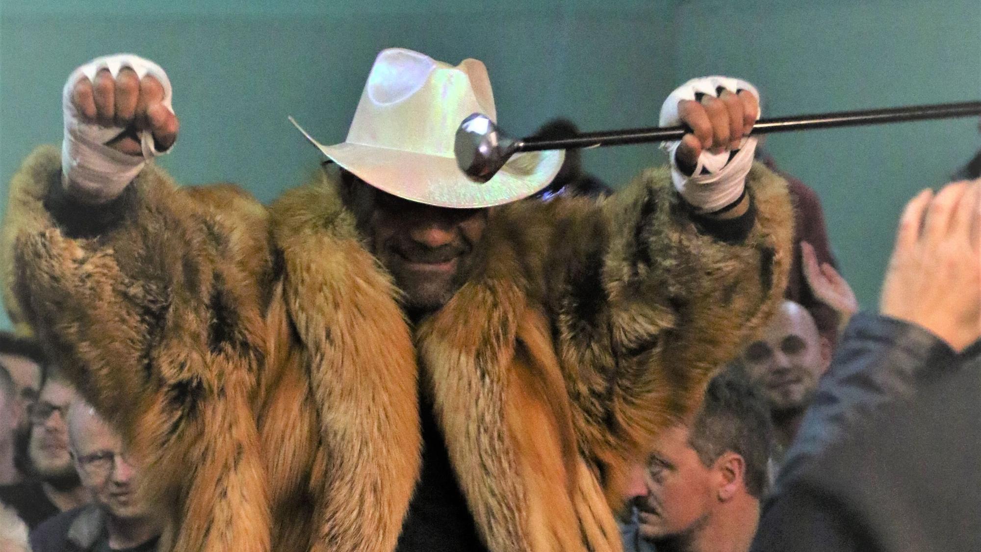 Remo Arns geht mit Cowboyhut und Pelzmantel mit erhobenen Armen durch die Menge bei der Mechernicher Fight Night. In einer Hand hält er einen Gehstock.