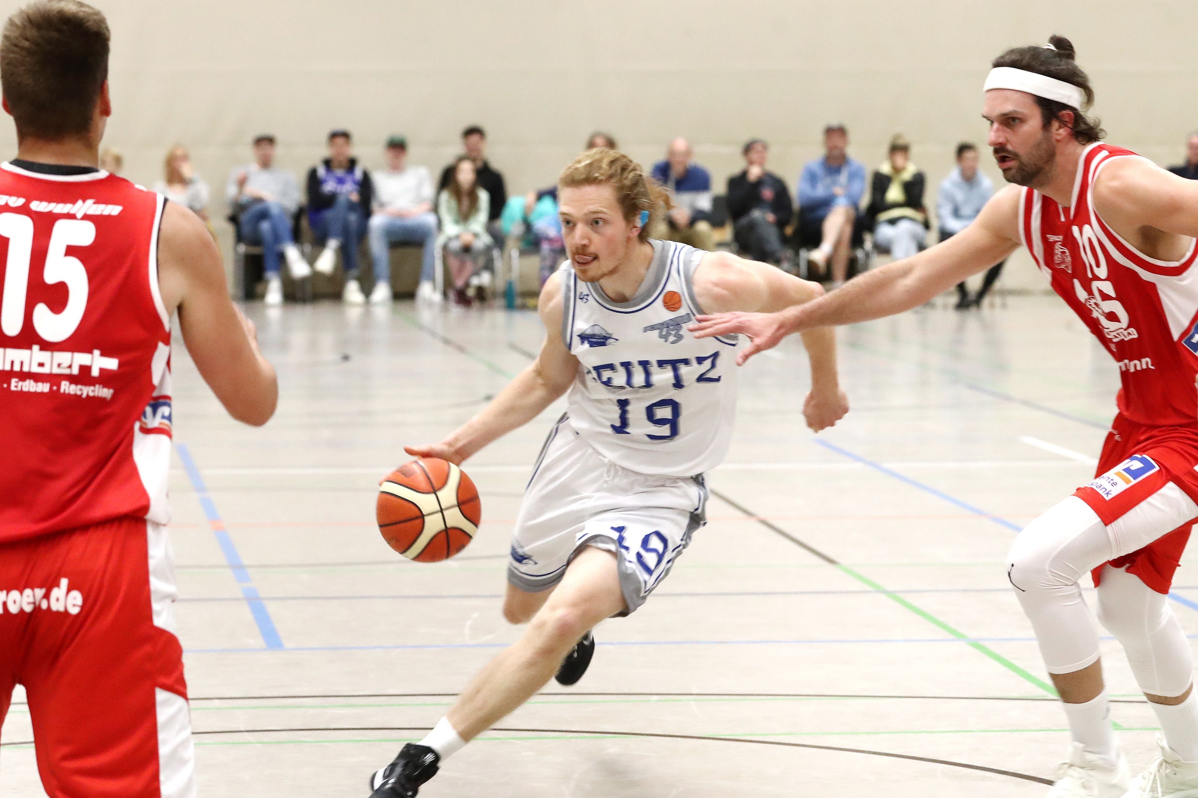 Ein Basketballspieler dribbelt an zwei Gegenspielern vorbei zum Korb.