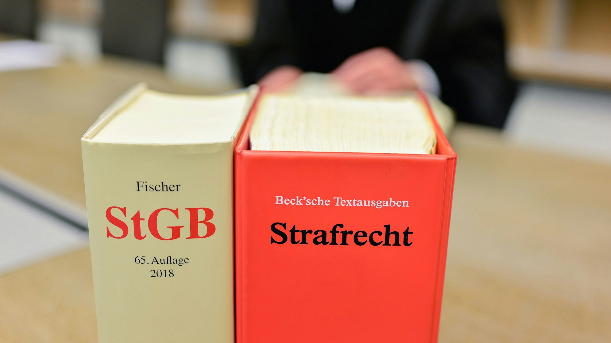 Ein Richter sitzt in einem Sitzungssaal des Gerichts hinter Büchern mit der Aufschrift „StGB“ und „Strafrecht“.