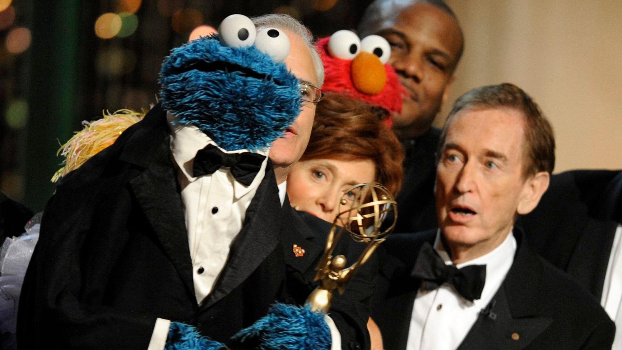 Schauspieler Bob McGrath steht im Smoking neben der Sesamstraßen-Figur Krümelmonster. Krümelmonster hält einen Preis, der für die Show bei einer Preisverleihung überreicht wurde.