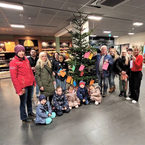 Frauen und Männer stehen im Kaller Rewe-Center an einem Weihnachtsbaum mit Wunschkarten und einige Kinder knien davor.