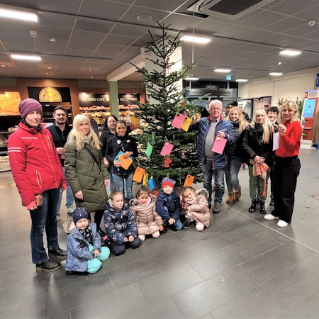 Frauen und Männer stehen im Kaller Rewe-Center an einem Weihnachtsbaum mit Wunschkarten und einige Kinder knien davor.