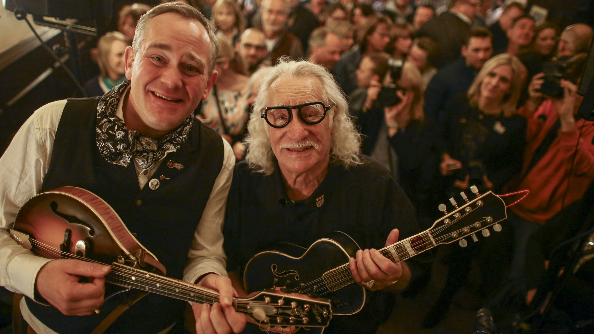 JP Weber und Hans Süper schauen mit ihren Mandolinen in den Händen in die Kamera, im Hintergrund Kneipen-Publikum.