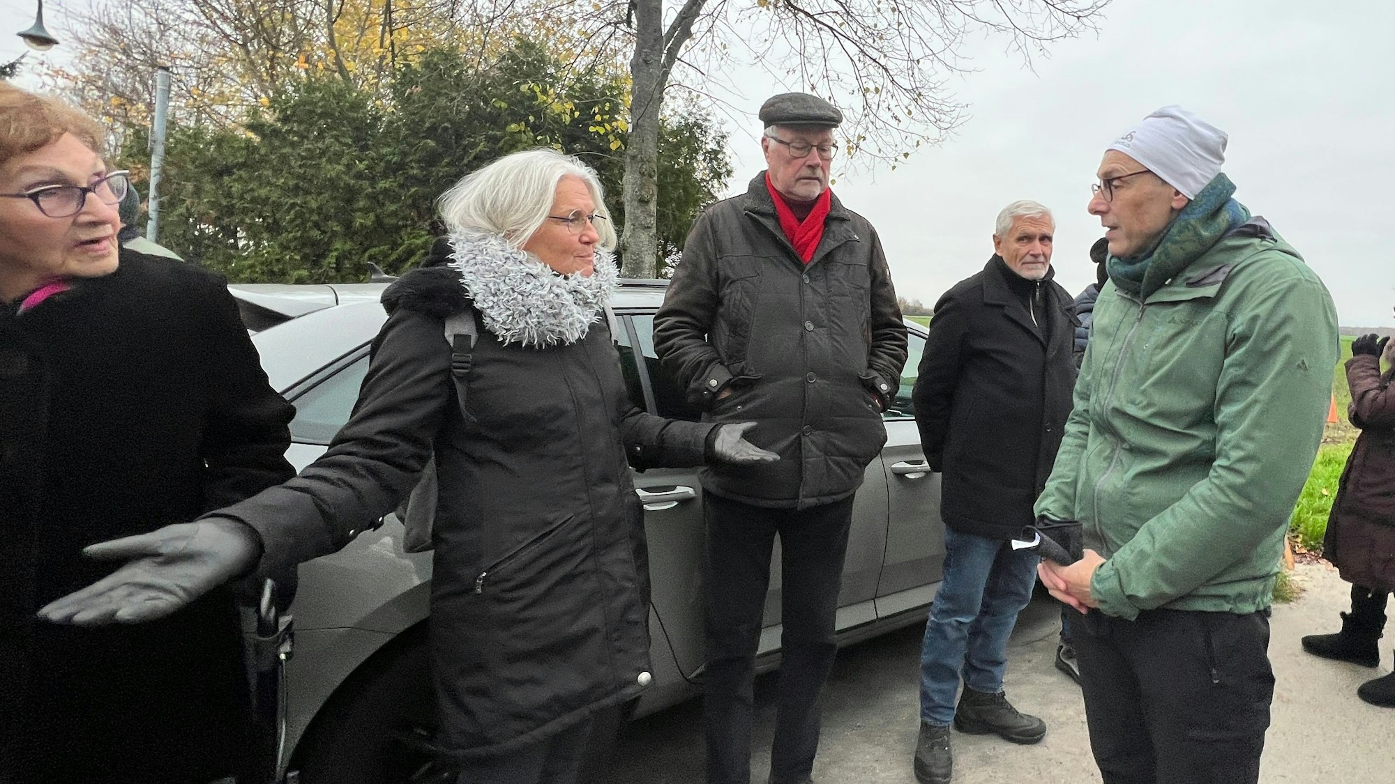 Fünf Menschen stehen in einer Gruppe zusammen. Eine Frau, Monika Thole, diskutiert mit ausgebreiteten Armen mit Jörg Lichter, der vor ihr steht.