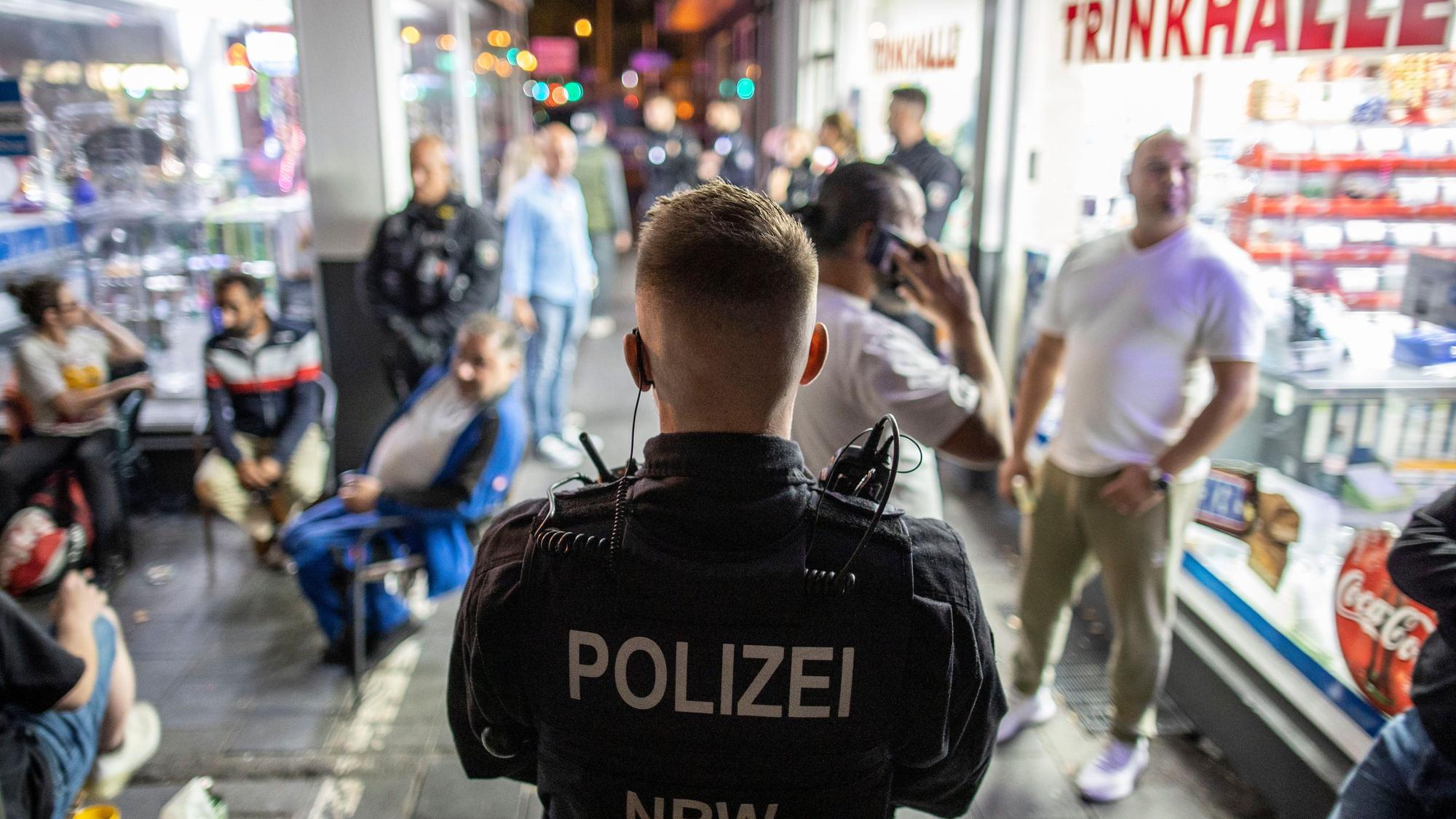 Ein Polizist steht im Zuge einer Razzia im Duisburger Norden am Freitagabend vor einer Trinkhalle und überwacht die Gäste des Lokals. Einsatzkräfte verschiedener Behörden durchsuchten in einer gemeinsamen Aktion gegen die Clan-Kriminalität 13 Objekte im Stadtgebiet und kontrollierten über 130 Personen, heißt es in einer Pressemitteilung.