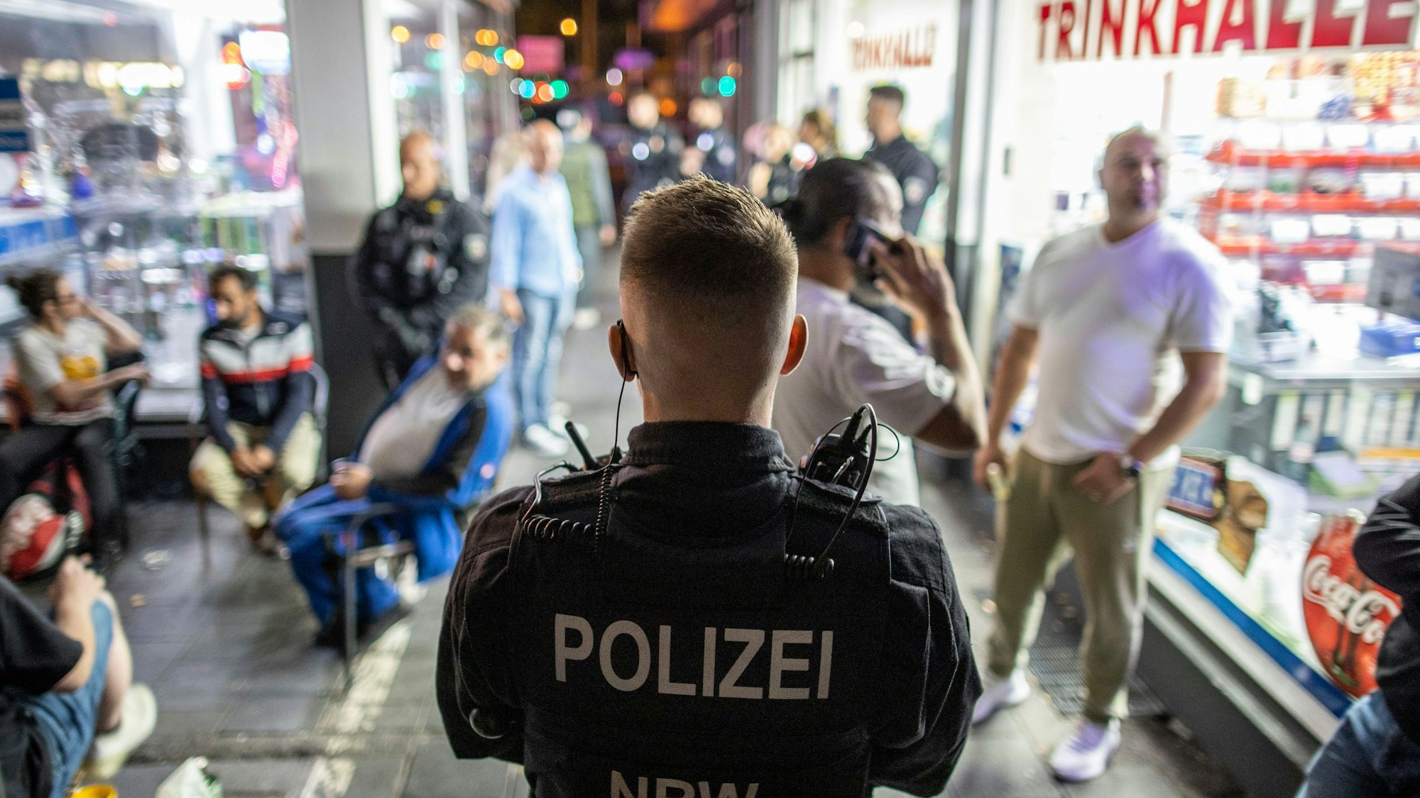 Ein Polizist steht im Zuge einer Razzia im Duisburger Norden am Freitagabend vor einer Trinkhalle und überwacht die Gäste des Lokals. Einsatzkräfte verschiedener Behörden durchsuchten in einer gemeinsamen Aktion gegen die Clan-Kriminalität 13 Objekte im Stadtgebiet und kontrollierten über 130 Personen, heißt es in einer Pressemitteilung.