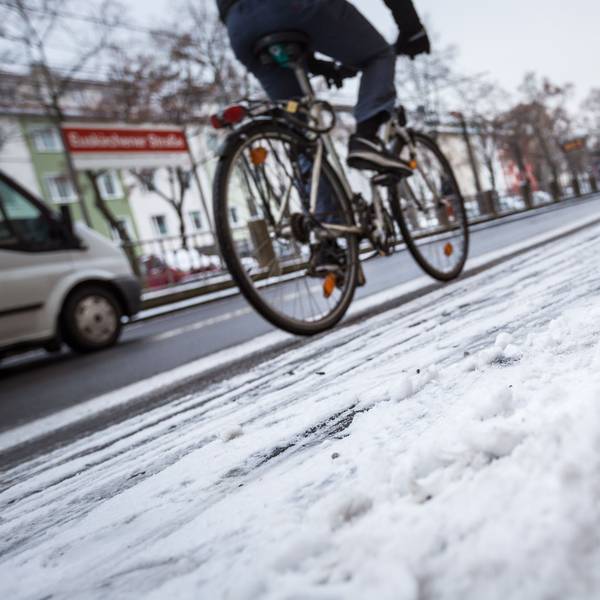 Schneematsch liegt auf einem Bürgersteig in Köln während ein Fahrradfahrer auf dem Radweg unterwegs ist.
