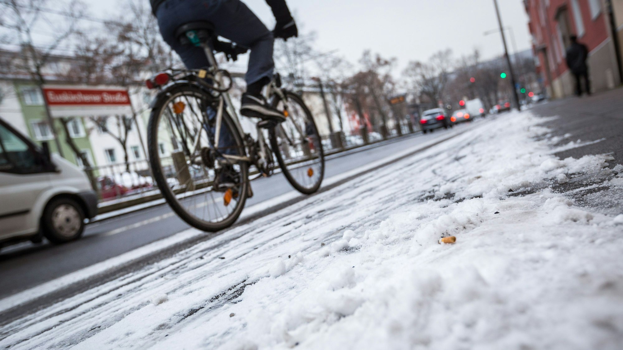 Schneematsch liegt auf einem Bürgersteig in Köln während ein Fahrradfahrer auf dem Radweg unterwegs ist.