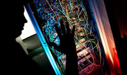 Ein Mann steht an einem Serverschrank aus dem ganz viele Kabel raushängen. - Symbolfoto zum Thema Kinderpornografie