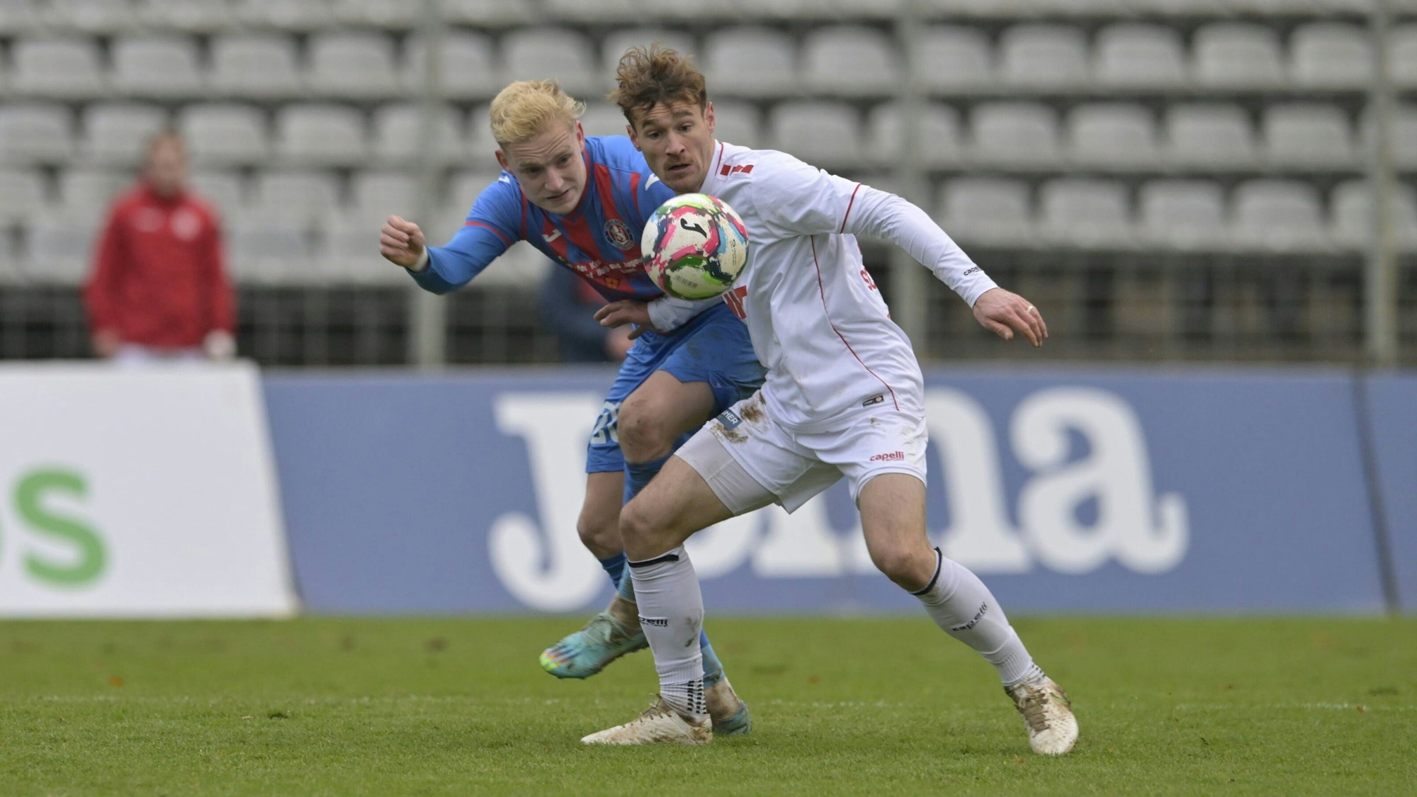 Zwei Fußballer im Zweikampf. Der vordere versucht, den Ball vor seinem Gegenspieler abzuschirmen.