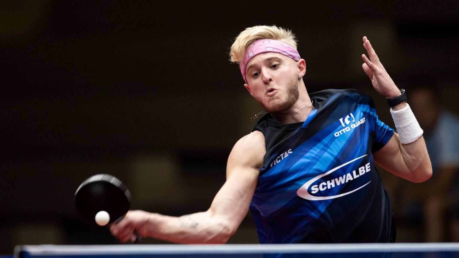 Zu sehen ist ein junger Tischtennisspieler, der den Ball mit der Vorhand über das Netz schlägt.