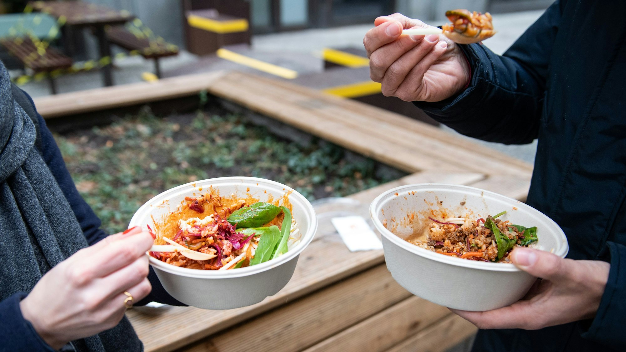 Ein Mann und eine Frau nehmen ihr Mittagessen aus einer Einwegverpackung zu sich.