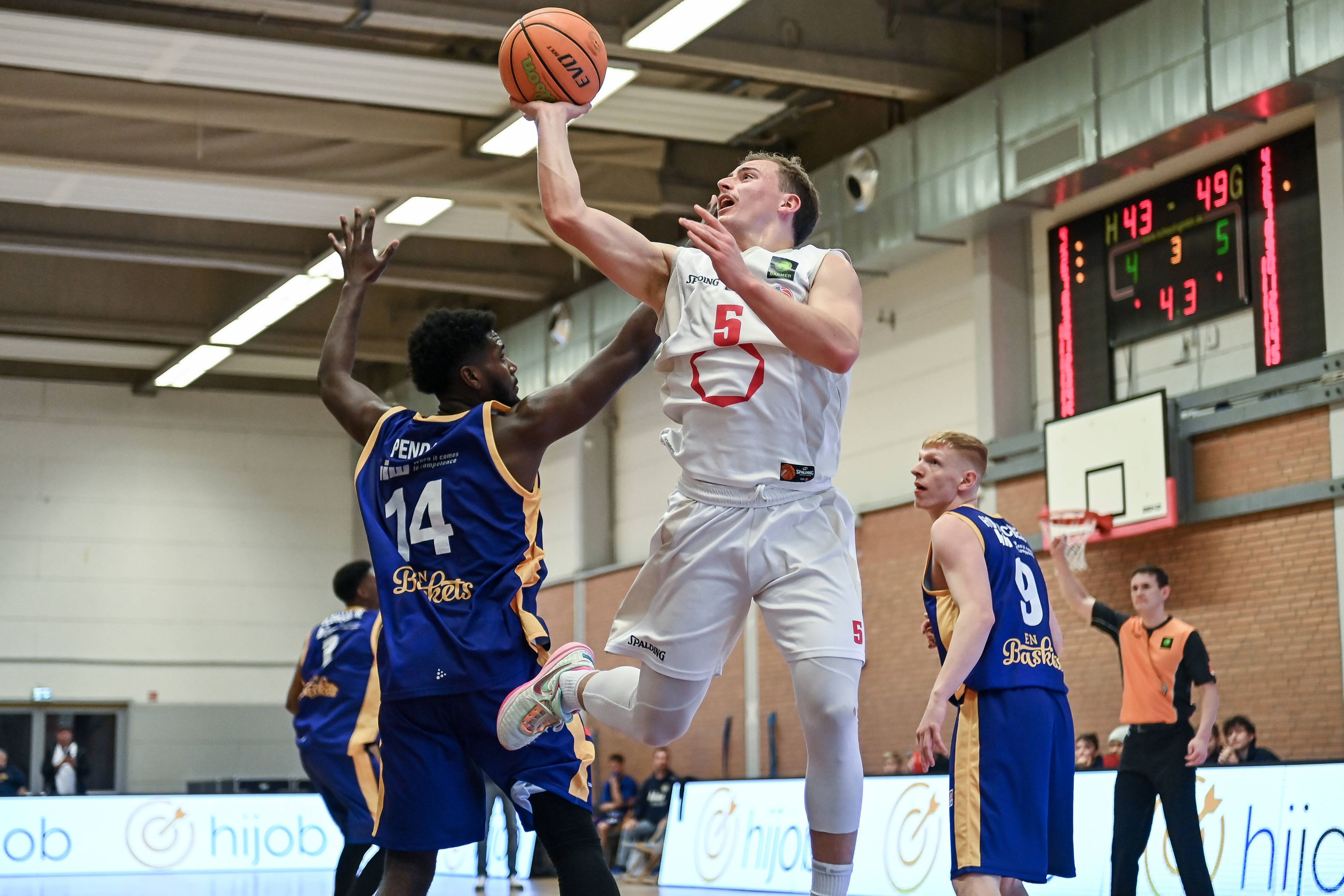 Ein Basketballer setzt sich gegen seinen Gegenspieler durch und wirft den Ball auf den Korb.