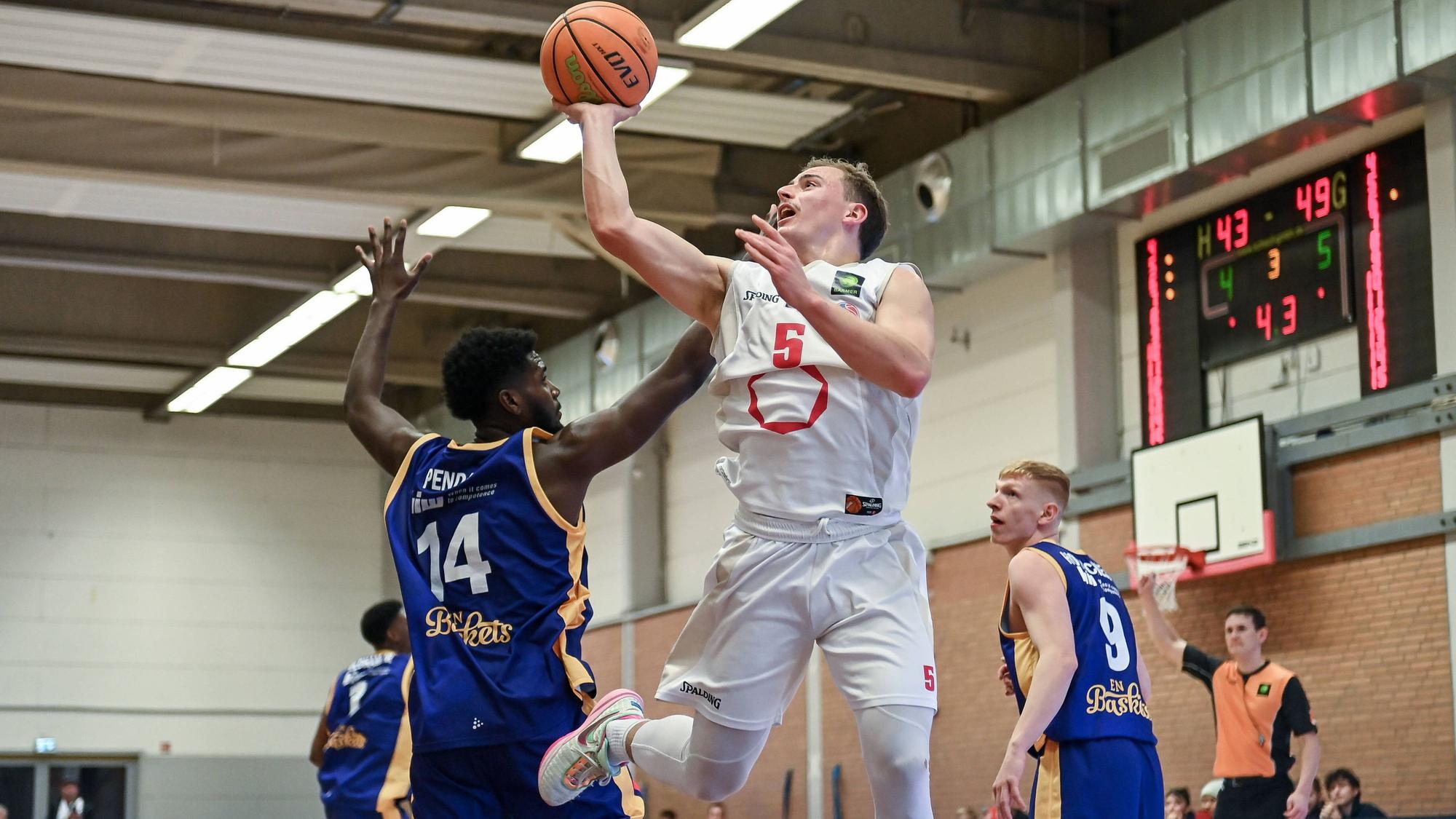 Ein Basketballer setzt sich gegen seinen Gegenspieler durch und wirft den Ball auf den Korb.
