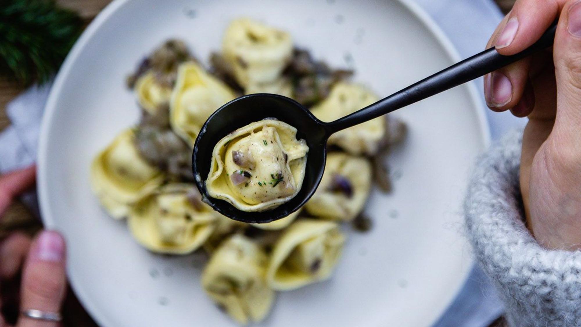 Waldige Tortellini di bosco liegen auf einem Teller und werden mit einem Löffel gegessen.