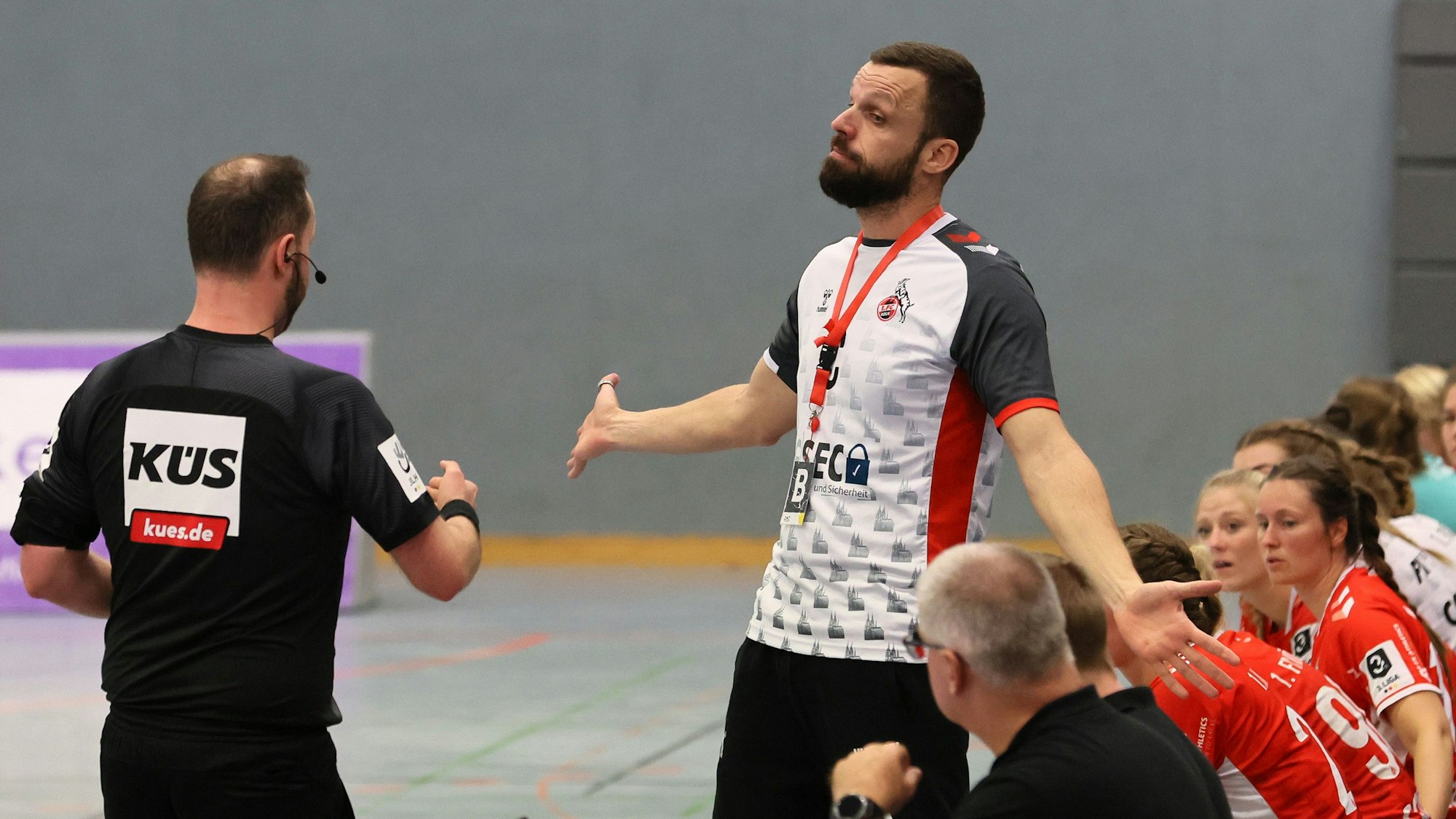 Ein Handballtrainer steht am Spielfeldrand, gestikuliert und diskutiert mit dem Schiedsrichter.