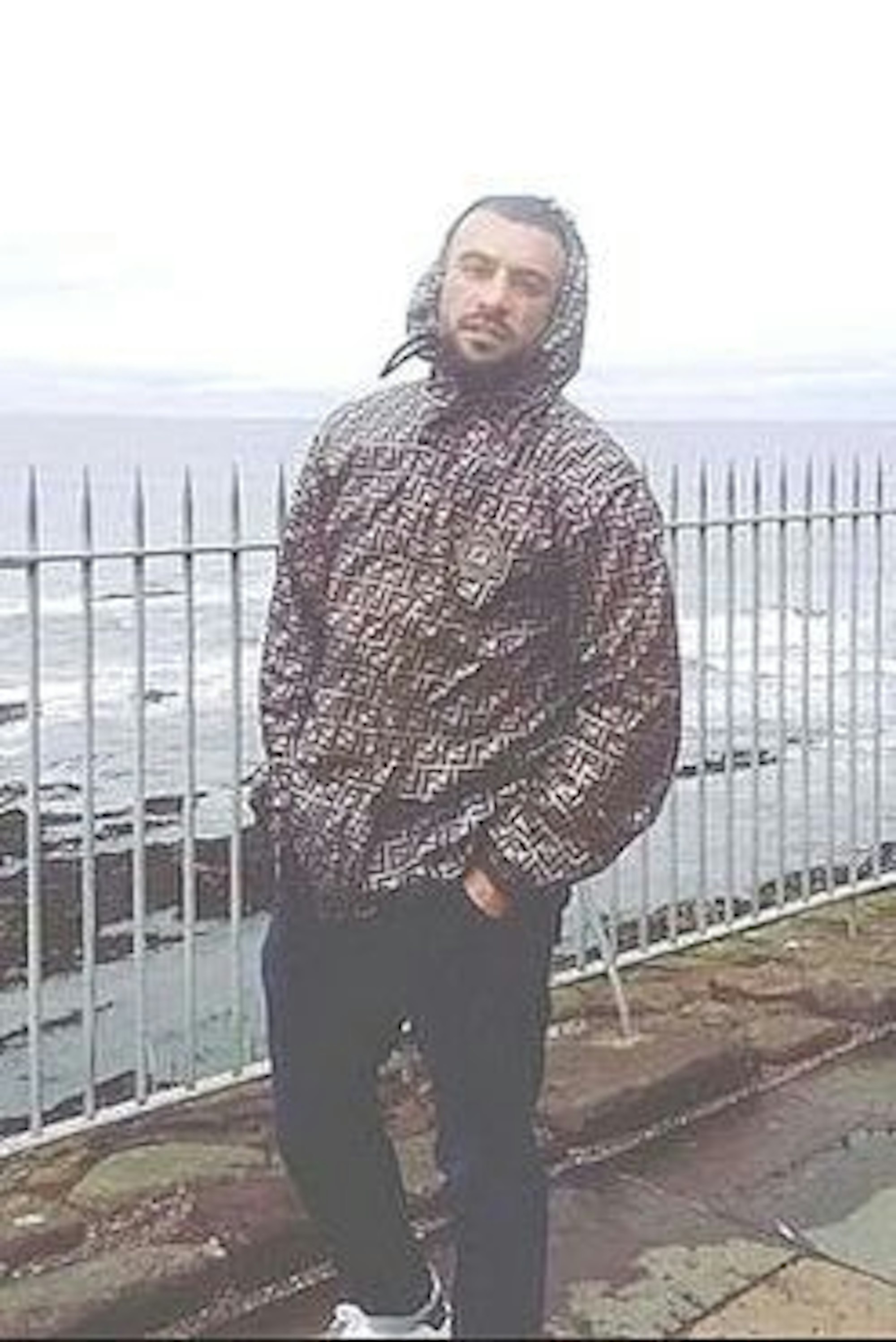 Tatverdächtiger steht vor einem Zaun, Wasser im Hintergrund.