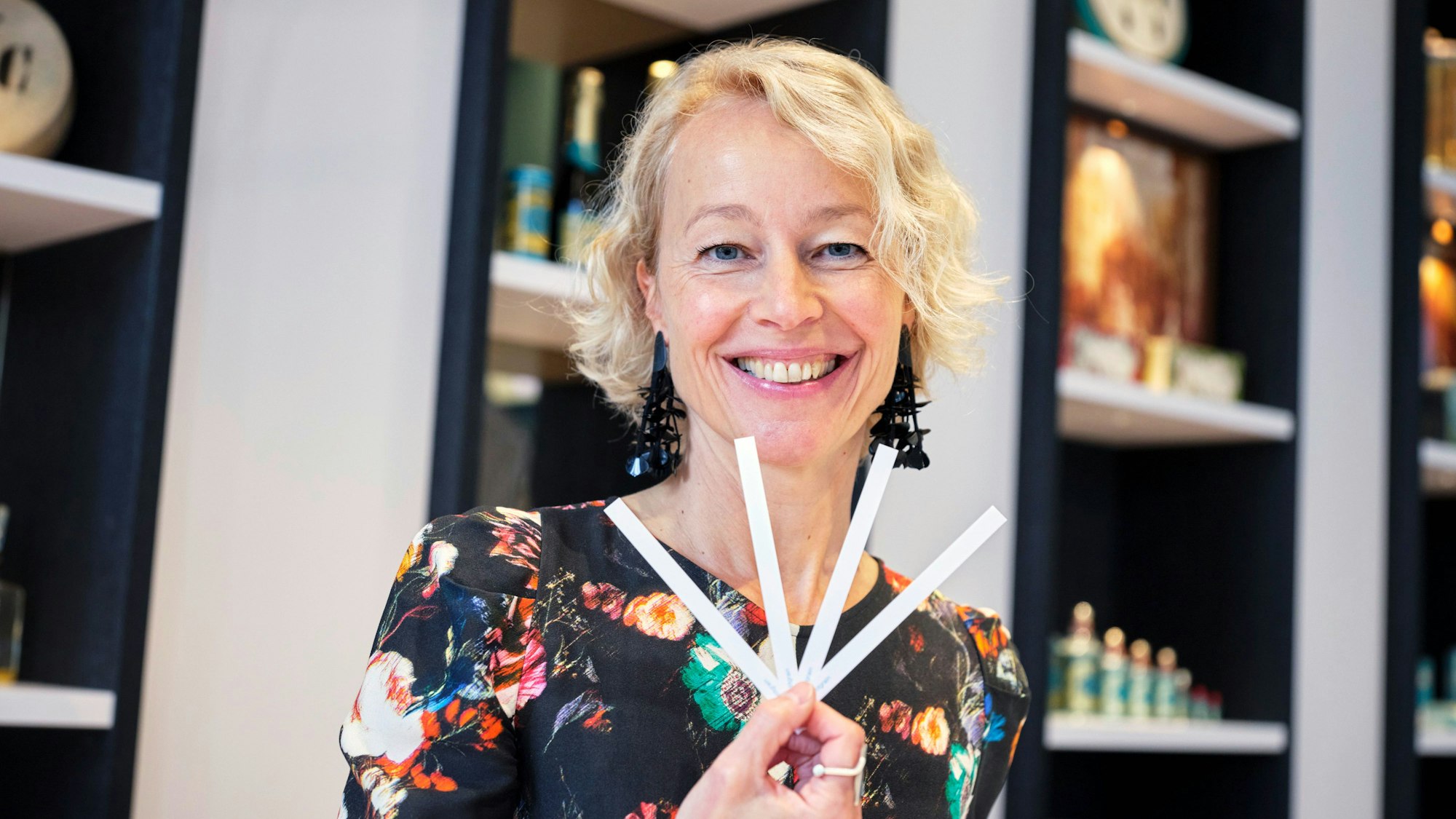 Alexandra Kalle hält vier weiße Stäbchen vor sich und lächelt in die Kamera. Sie trägt ein dunkles Top mit buntem Blumenmuster.