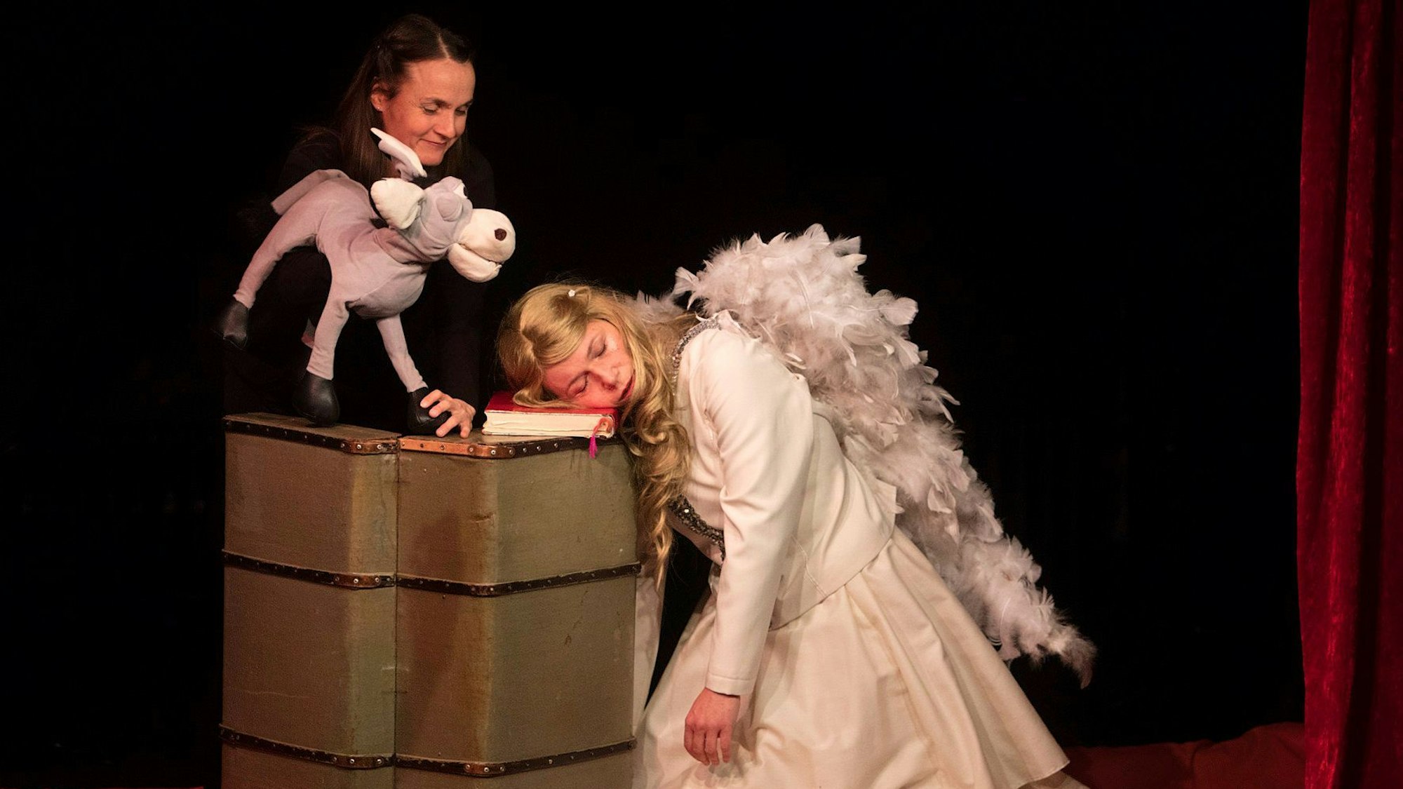 Ein Engel ist auf einem Buch eingeschlafen, eine Puppenspielerin bewegt einen Esel, der zum Engel schaut