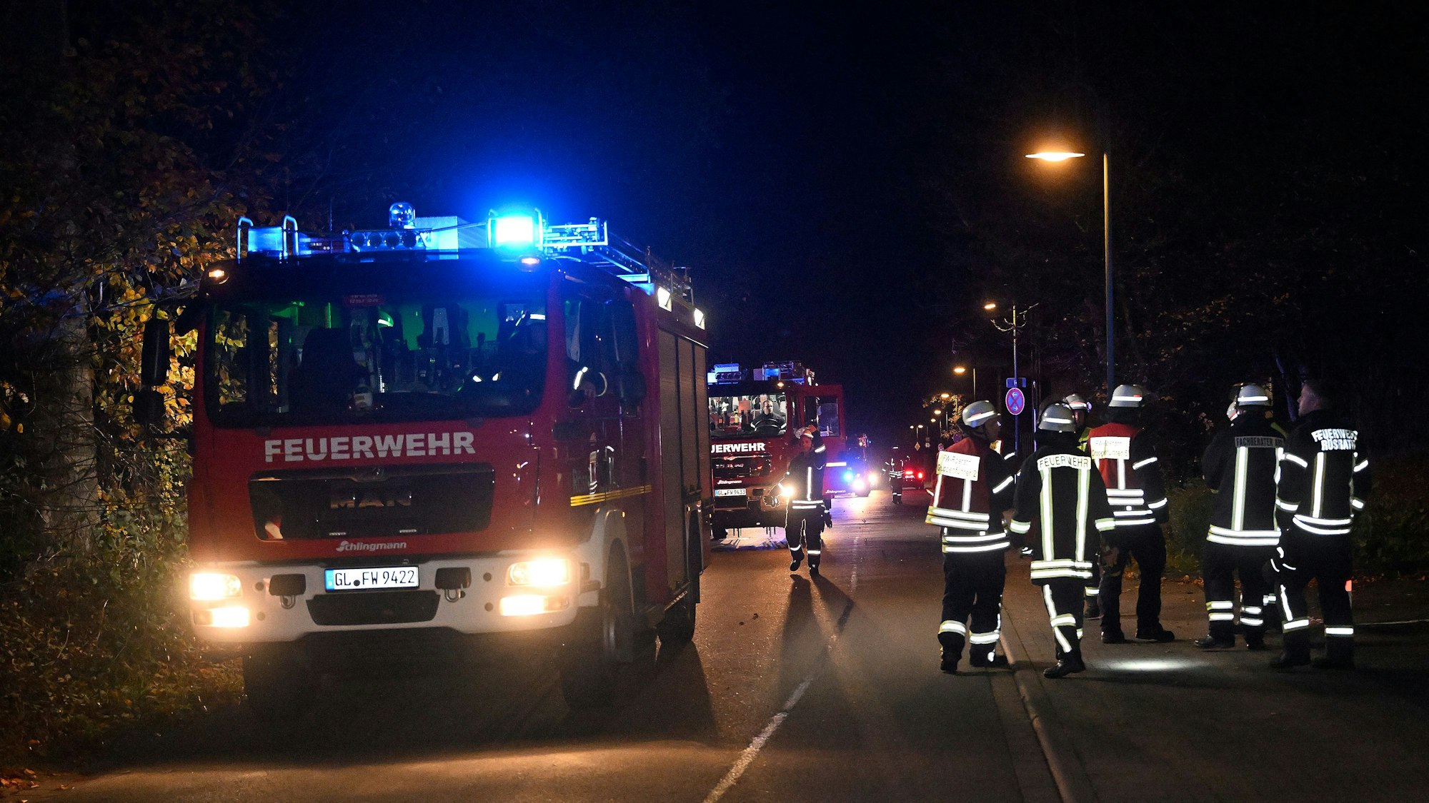 Zwei Feuerwehrautos und mehrere Feuerwehrkräfte stehen nachts an einem Einsatzort.