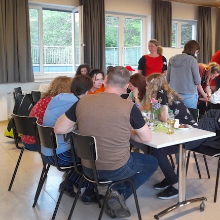 Café International des Fluchtpunkts Kürten: An mehreren längeren Tischen sitzen Menschen verschiedener Nationen und unterhalten sich.