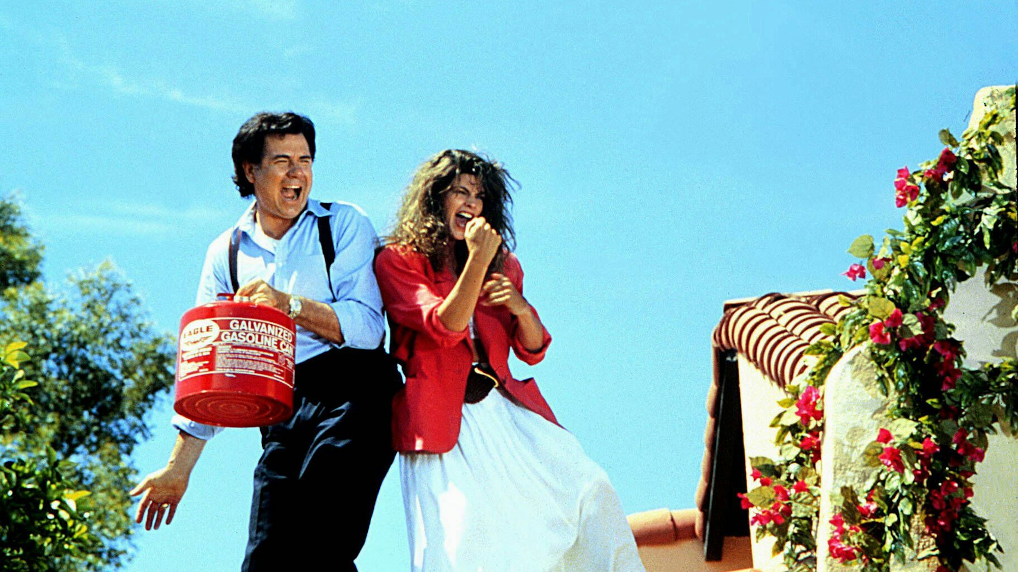 John Larroquette und Kirstie Alley auf dem Dach ihres Hauses. Er hat einen Kanister Benzin in der Hand. Sie die Streichhölzer.